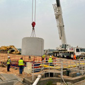 Construction site with a crane lifting a giant cement part for sewer lines in a sewage treatment plant