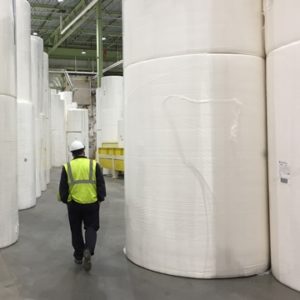Engineer in PPE walking through warehouse of giant reams of tissue paper